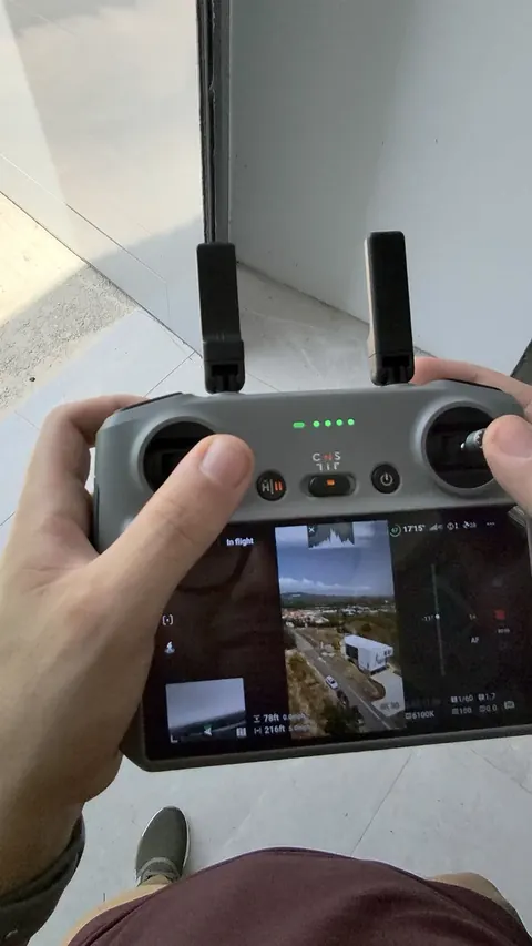 Hands holding the drone controller, with the live aerial view on the screen