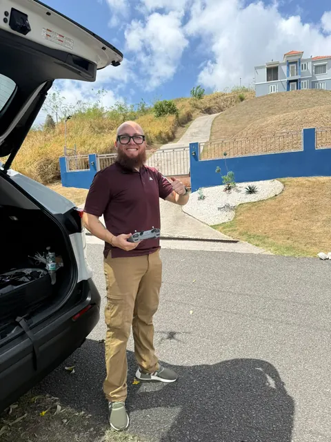 Justin from Ground Sky Studios smiling, drone controller in hand, next to his car